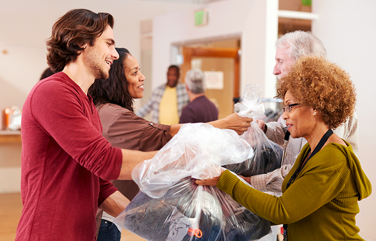 People Donating Clothing To Charity Collection In Community Center