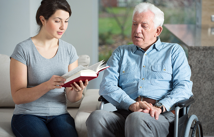 Senior care assistant reading book to elderly man