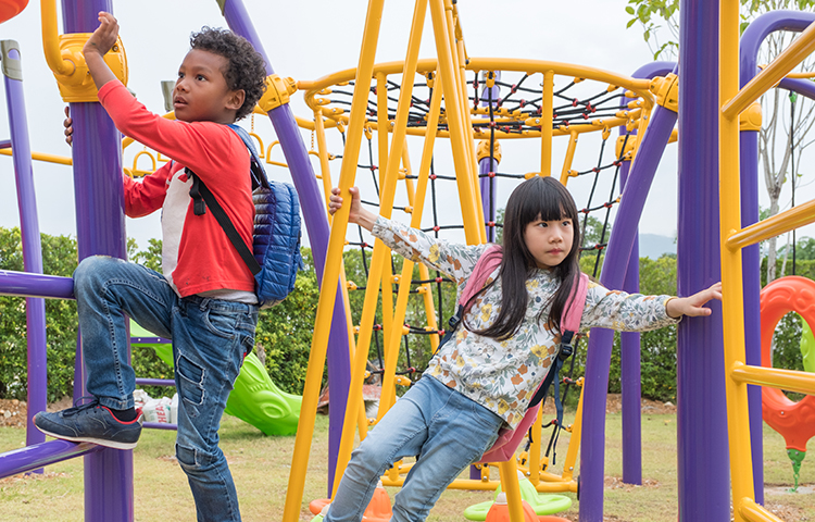 Two kids, a boy and girl, playing on children's climbing toy at school playground