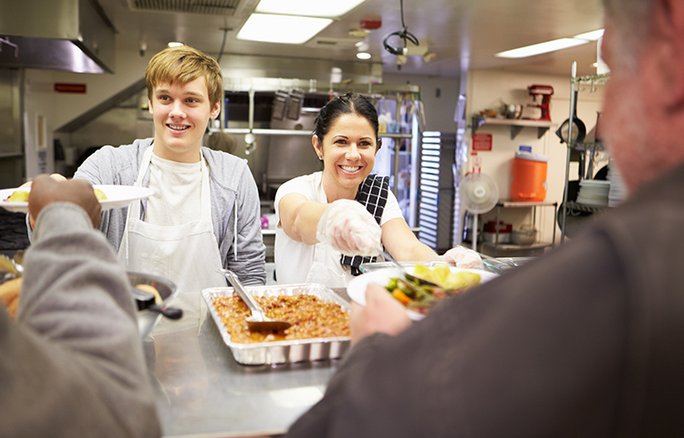 Staff Serving Food In Homeless Shelter Kitchen